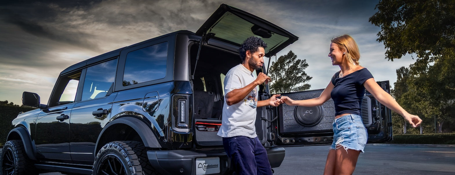 Two people standing next to a black SUV with an open door on a road.