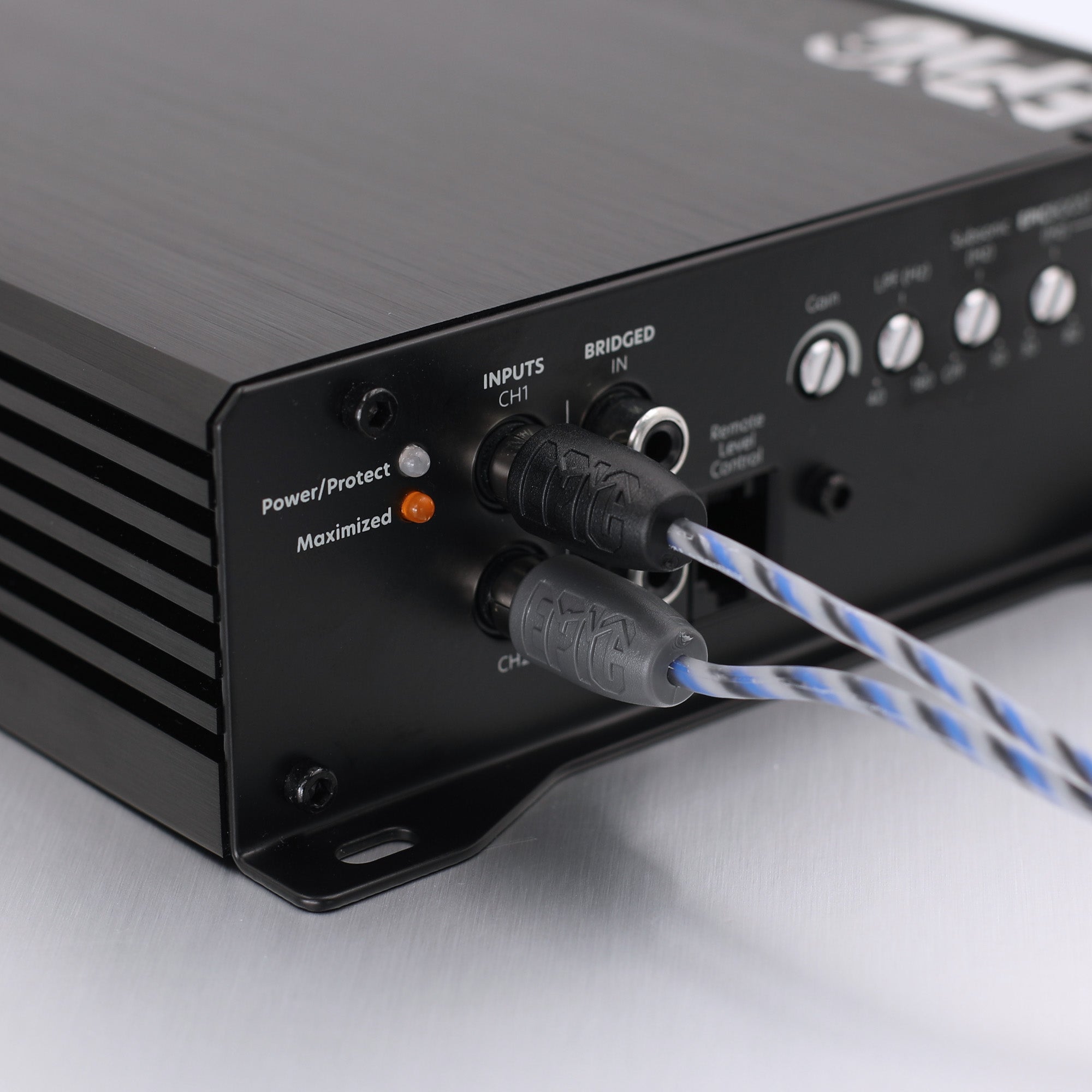 Close-up of a black audio amplifier or receiver rear panel with input jacks, control knobs, and blue-and-white cable connectors plugged in, photographed on a light gray surface.