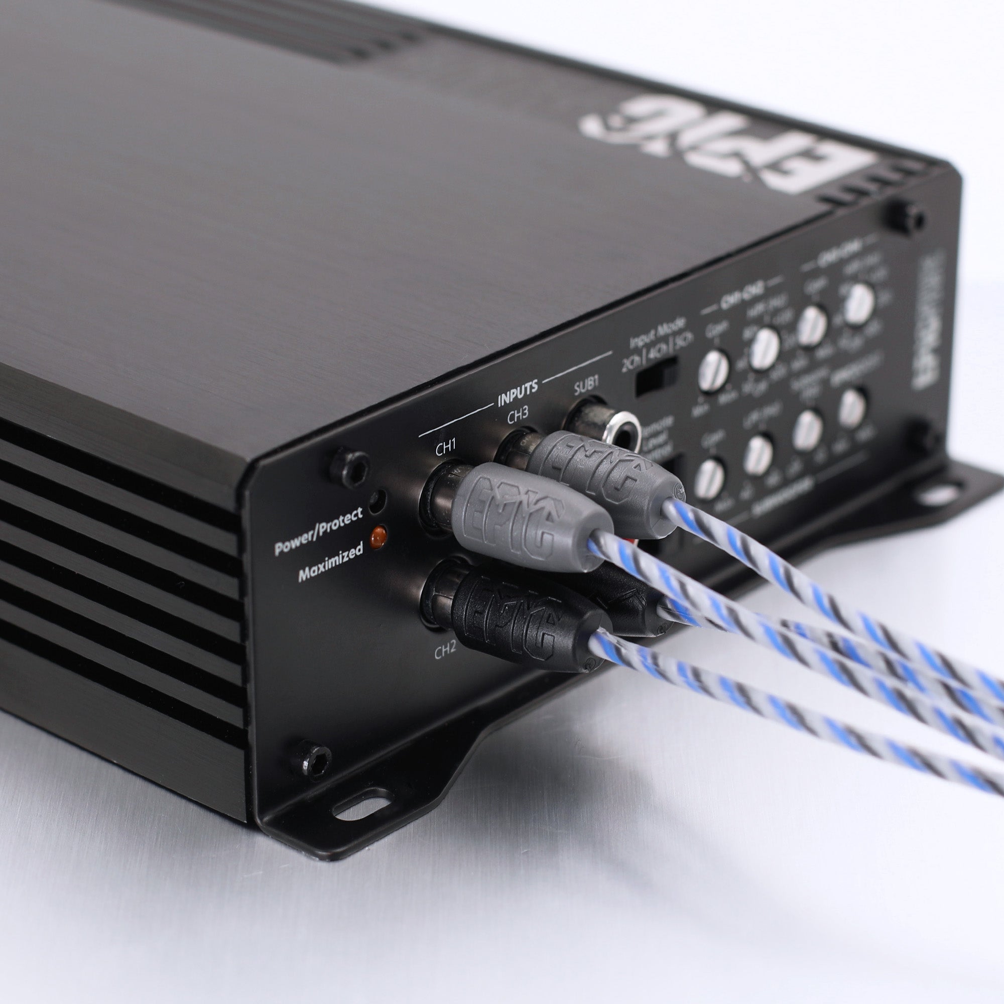 Close-up of the rear panel of a black audio power amplifier, showing input jacks, control knobs, and blue-and-white braided cables plugged in on a white background.