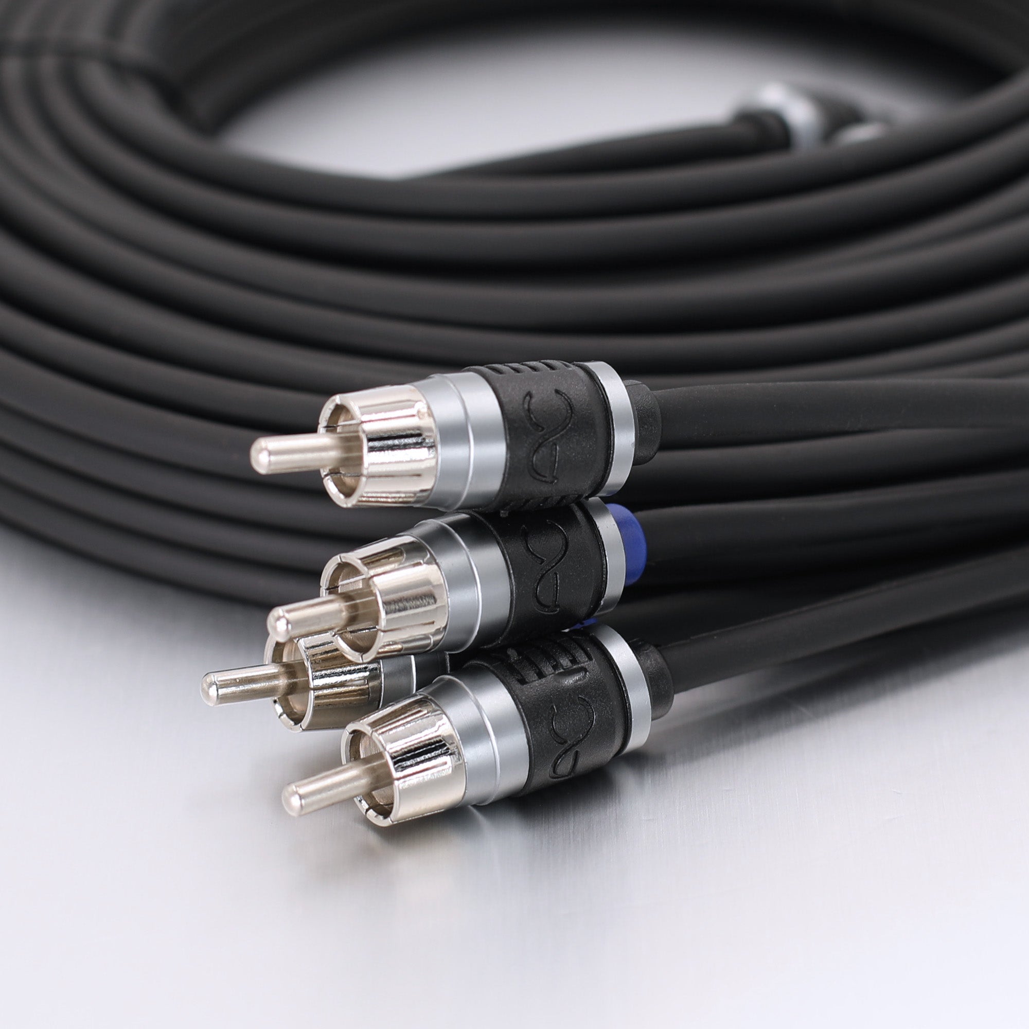 A close-up of a coiled black audio or video cable with four RCA-style connectors in the foreground, showing silver metal contacts and black-and-silver housings on a light gray surface.
