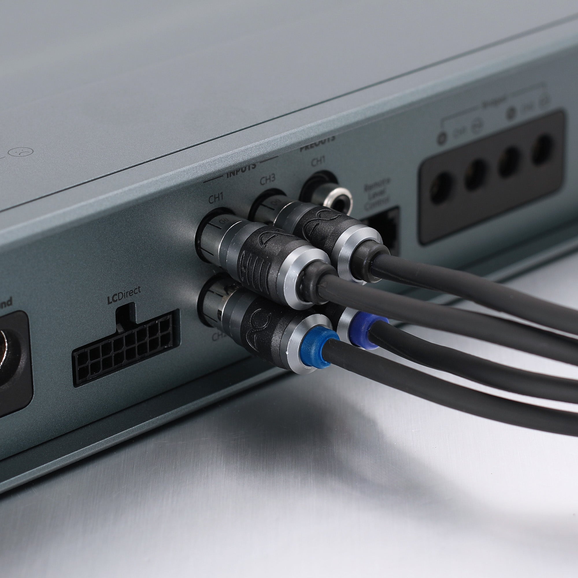 Close-up of audio or signal cables connected to the rear panel of a silver electronic device, showing XLR-style connectors and cable ties on a metallic surface.