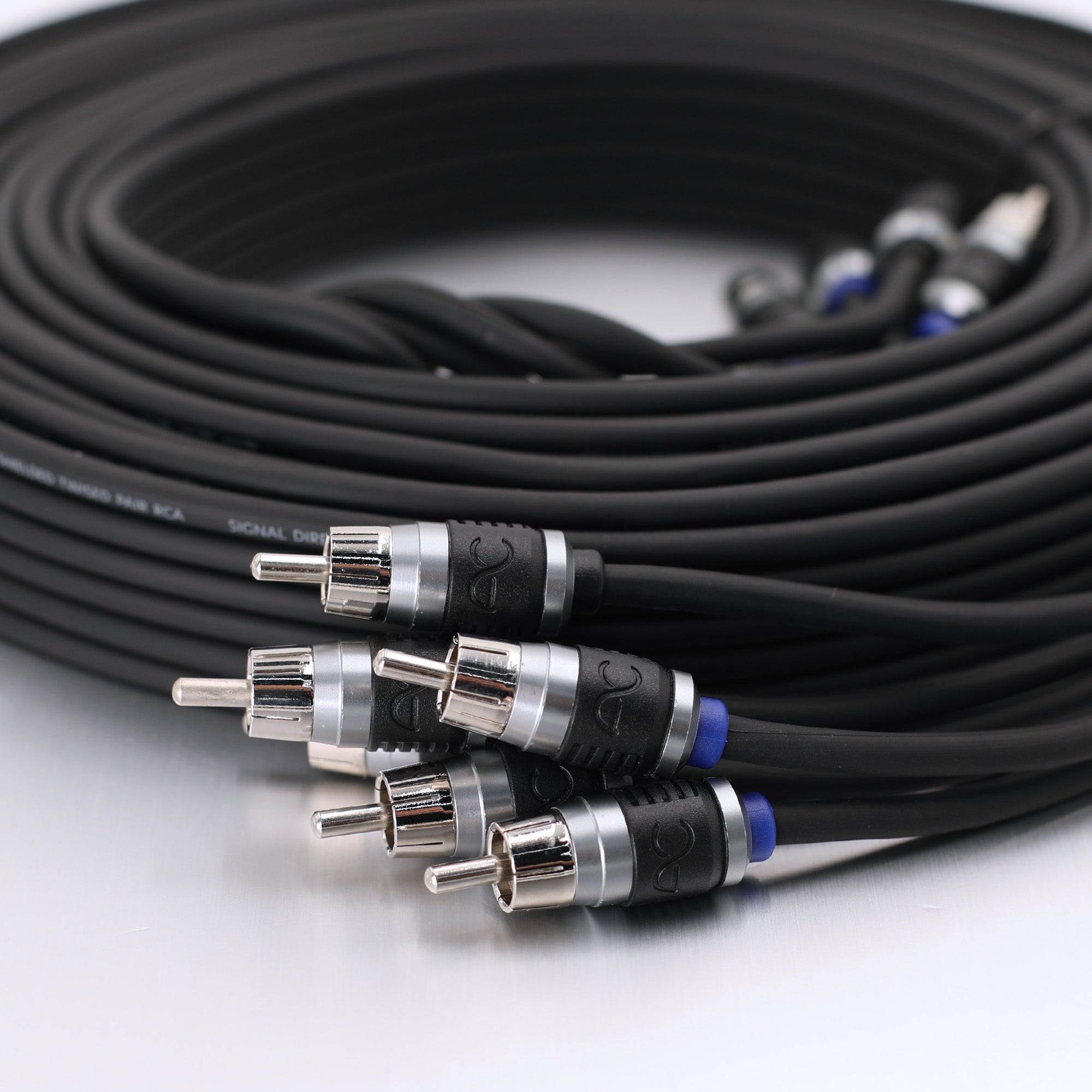 A coiled black audio cable with multiple RCA connectors in the foreground, photographed on a clean white surface.