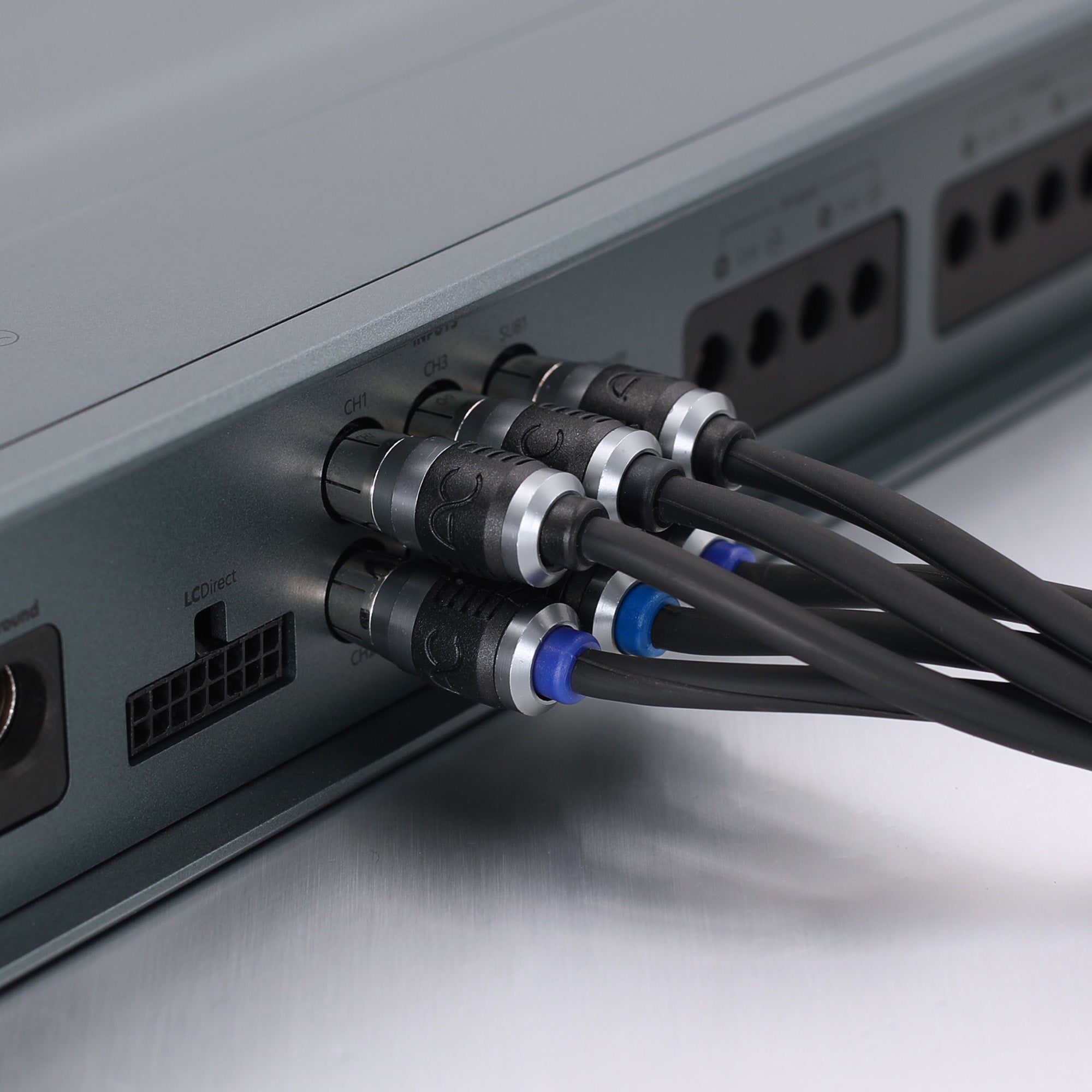 Close-up of audio or video cables plugged into the rear panel of a gray electronic device, showing black cables with silver connectors and blue ring accents.