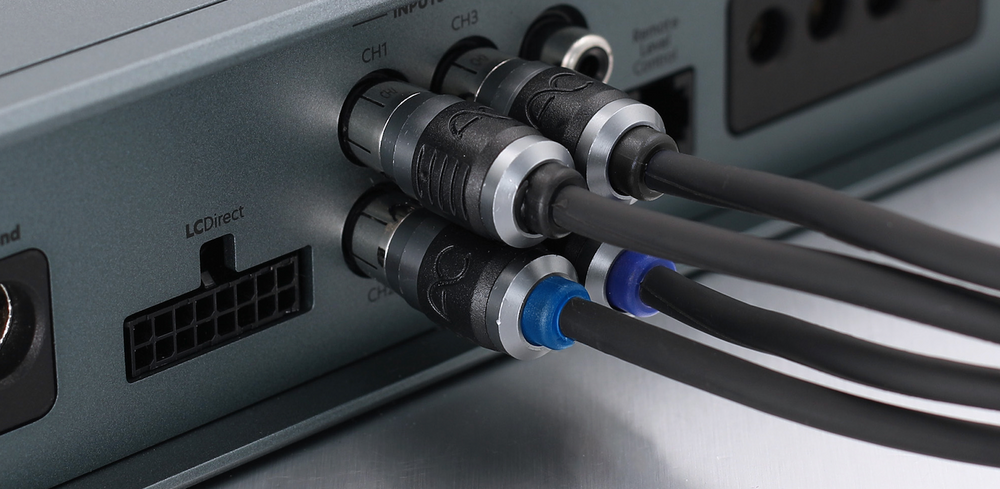 Close-up of audio or video cable connectors plugged into a device panel, with black cables and silver connector housings, plus one blue cable tie.