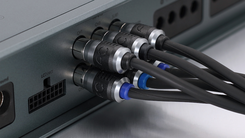 Close-up of multiple black audio or cable connectors plugged into the rear panel of a gray electronic device, with cables running toward the right on a metallic surface.