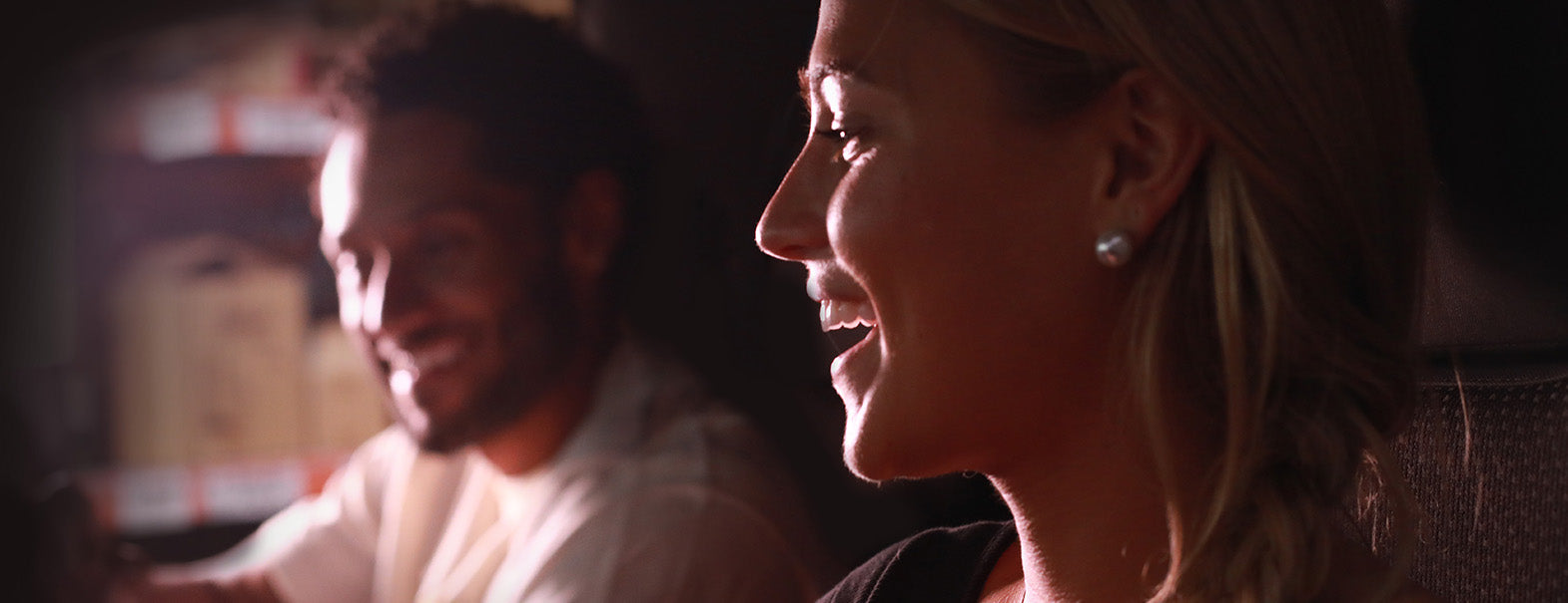 Two people sitting close together, one smiling, in a dimly lit setting.